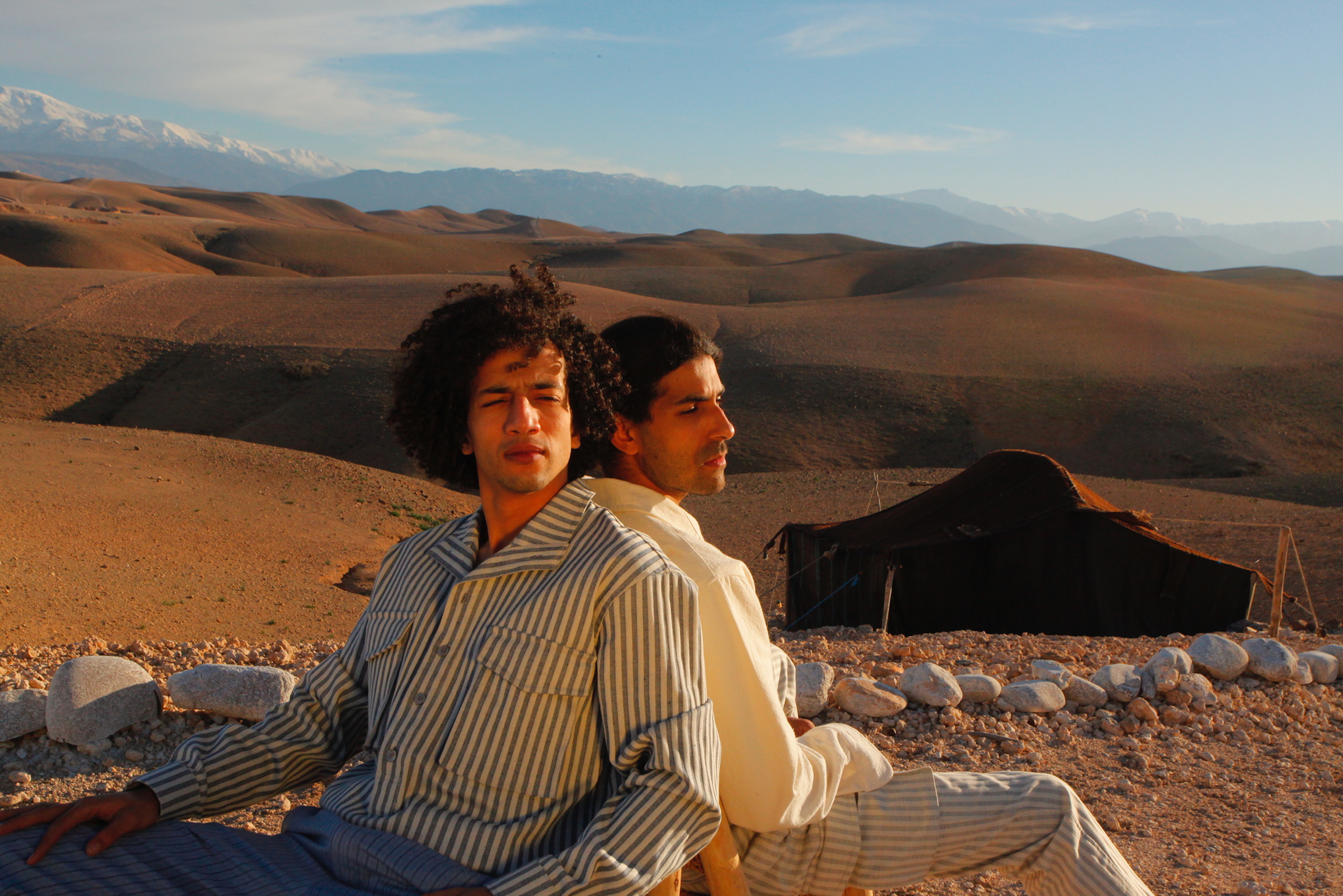 Two friends sitting in the Agafay desert at golden hour, Atlas Mountains in the distance